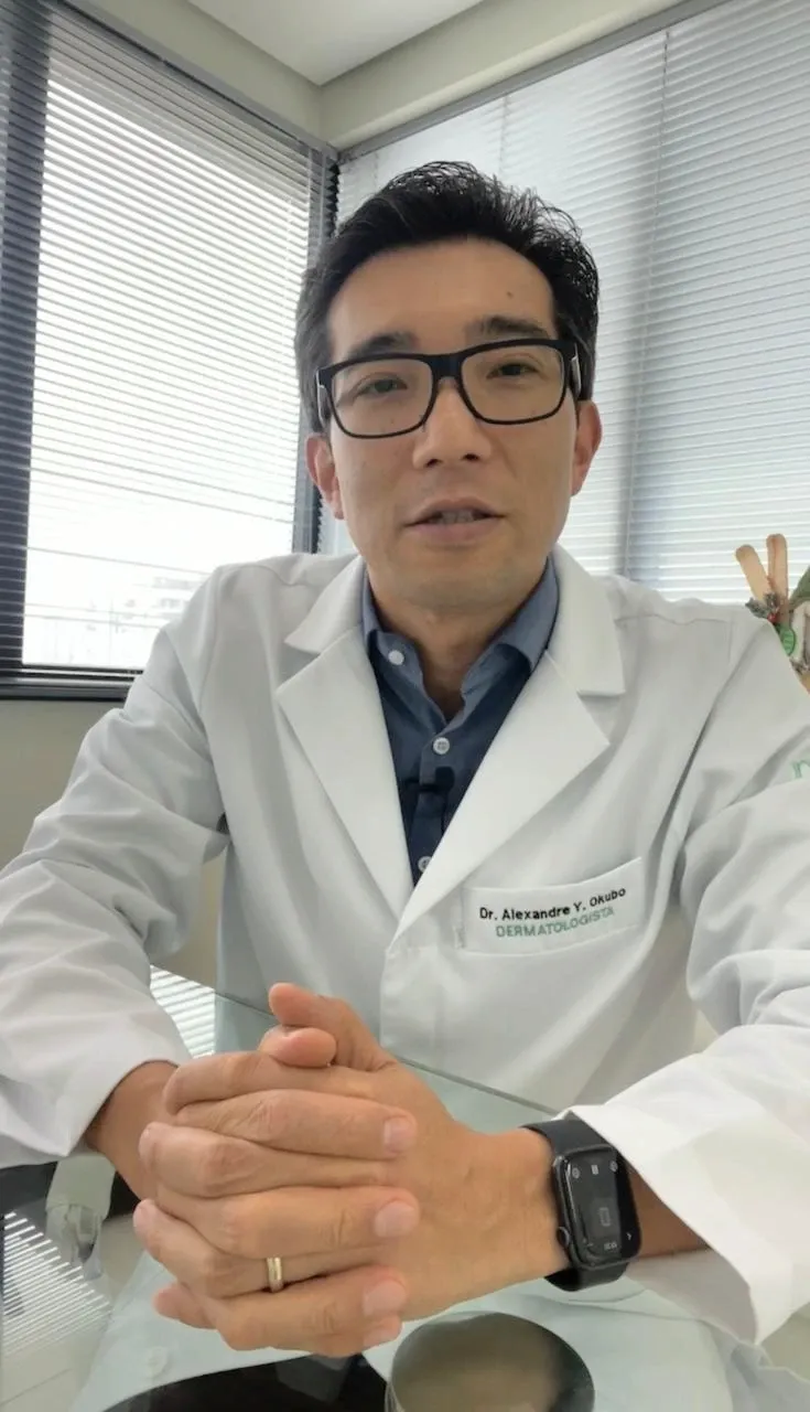 Dr. Alexandre Okubo conversando durante a consulta, sentado à mesa do consultório