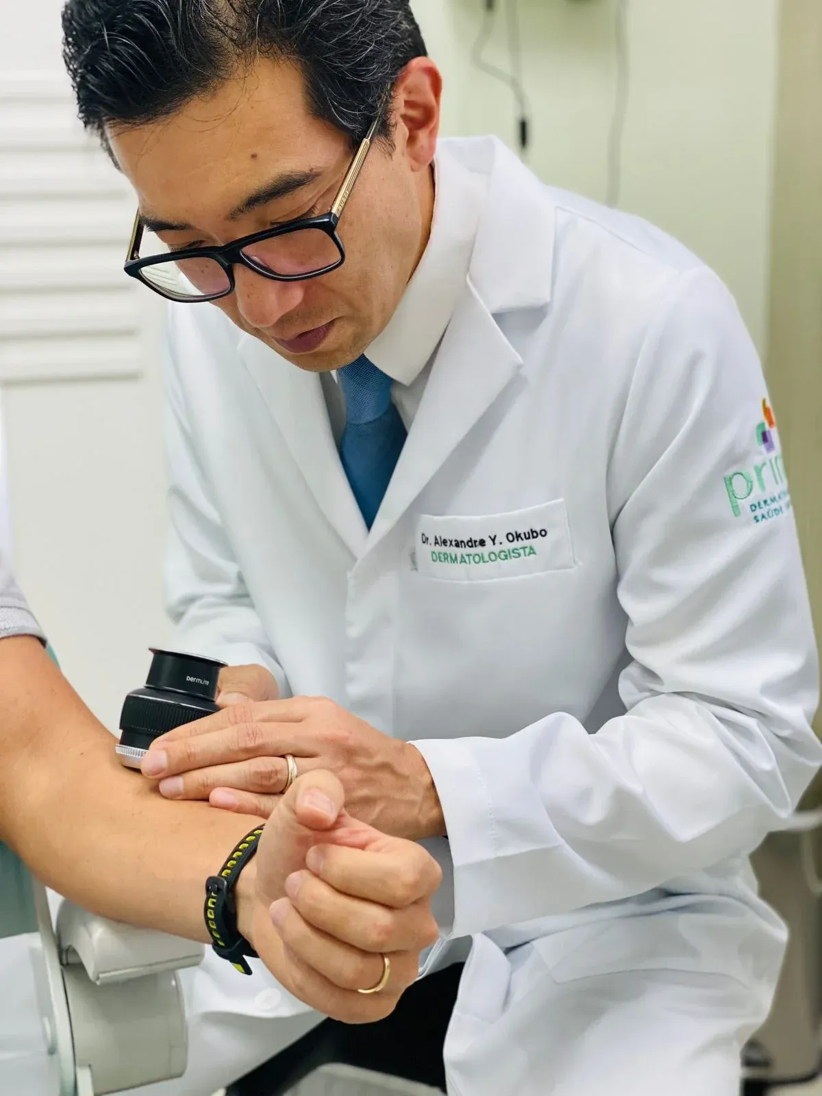 Dr. Alexandre Okubo, dermatologista, examina o braço de um paciente com dermatoscópio na Prime Dermatologia, em São Paulo